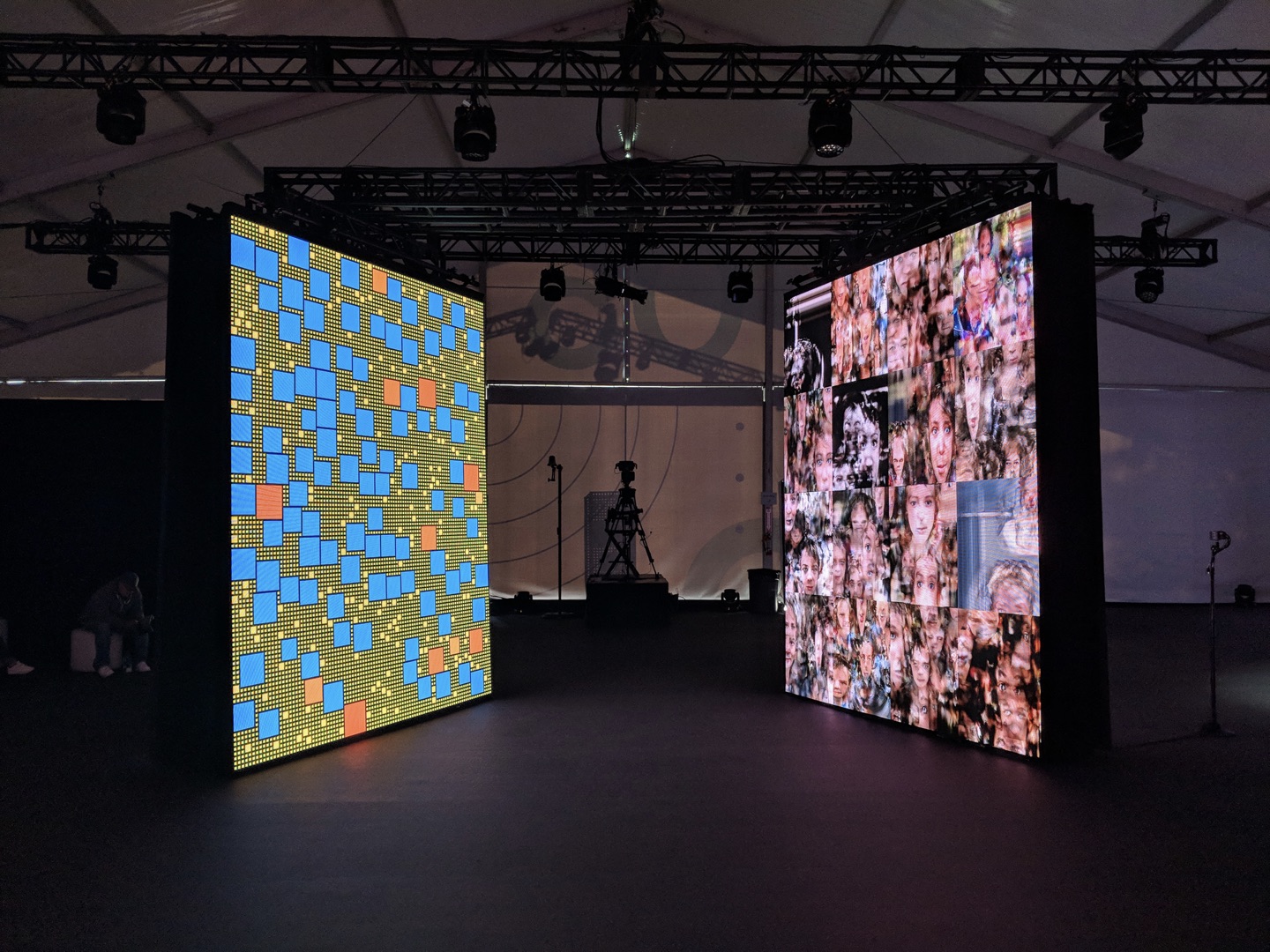 Two large LED screens, one with a colorful block pattern, another with odd faces.