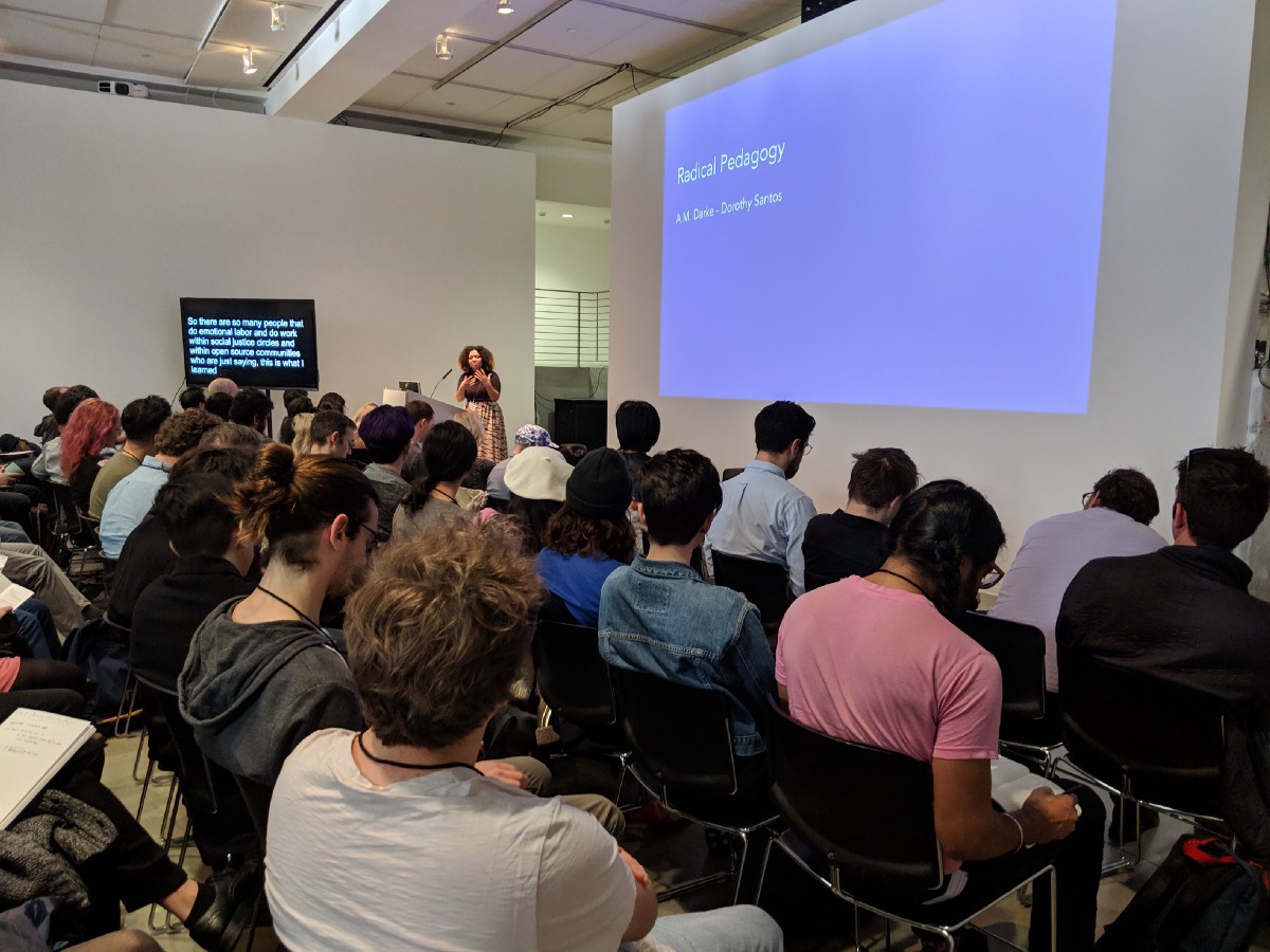 A woman giving a presentation to a full room in front of a screen that reads 'Radical Pedagogy.'