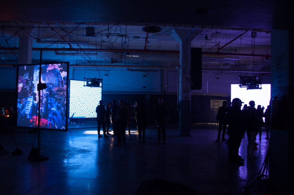 People standing in a dark room looking at media art projections on large screens.